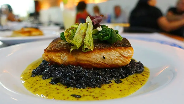 Plato de pescado presentado sobre arroz oscuro y salsa